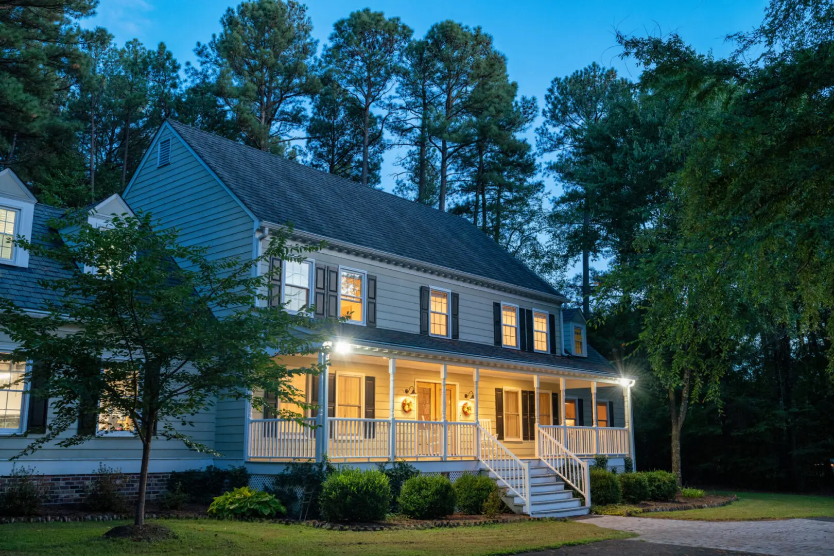 Illuminated house surrounded by trees at dusk.
