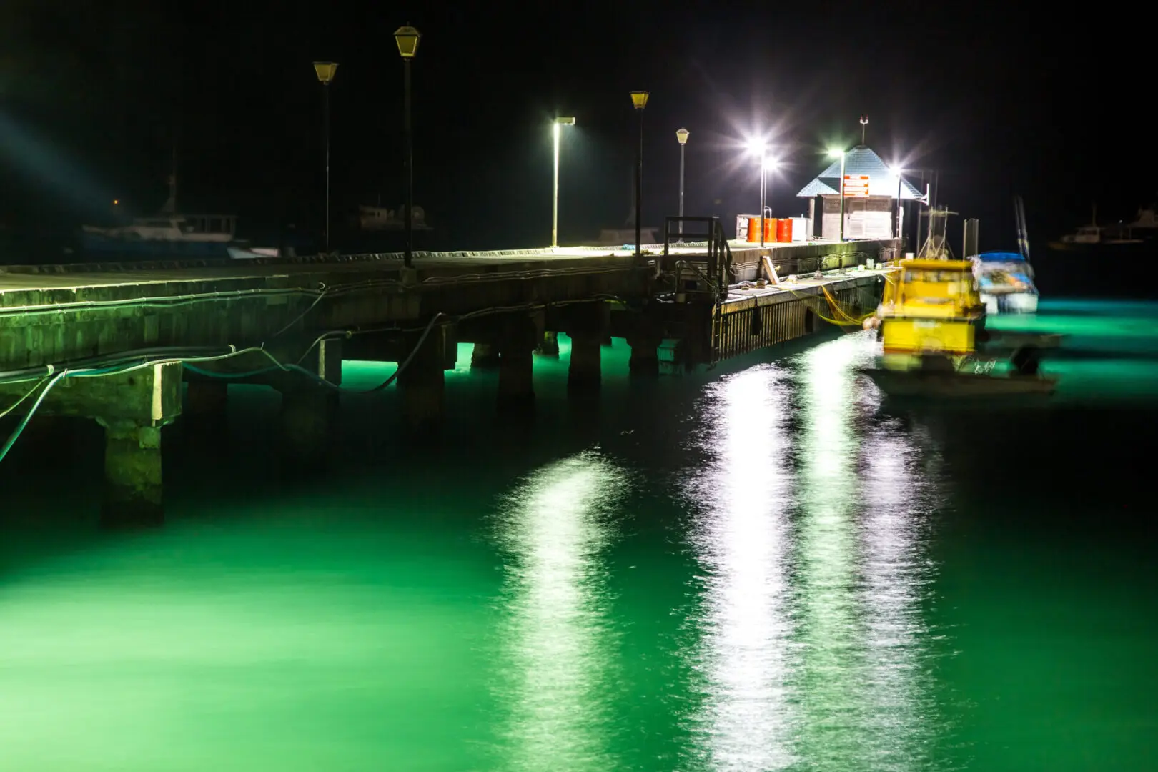 Lit pier over glowing green water at night.