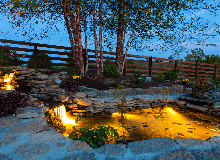 Illuminated garden pond with cascading waterfall.