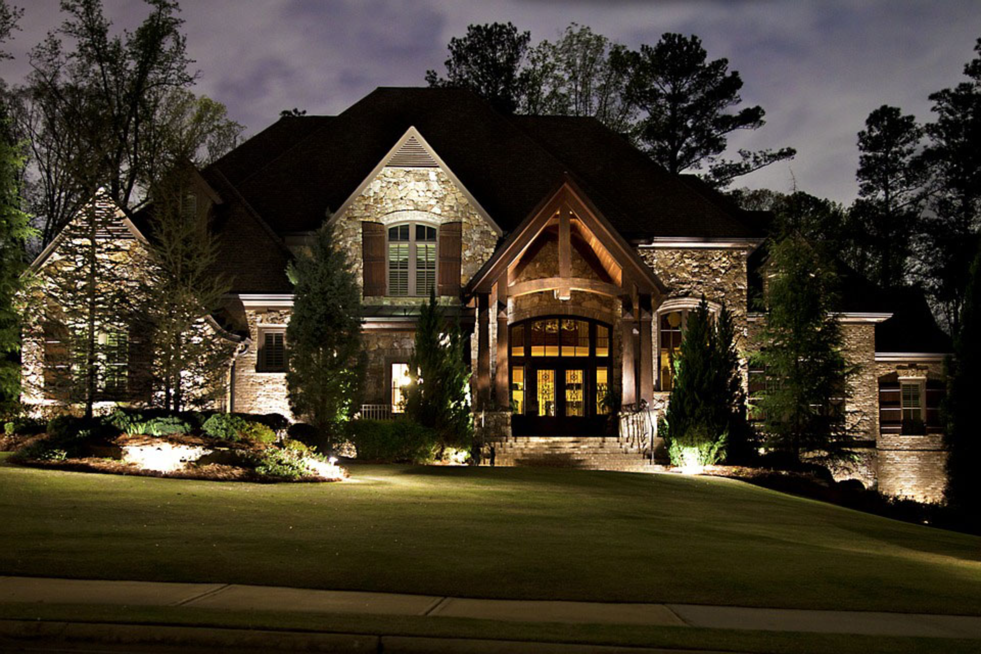 Illuminated stone house surrounded by trees at night.