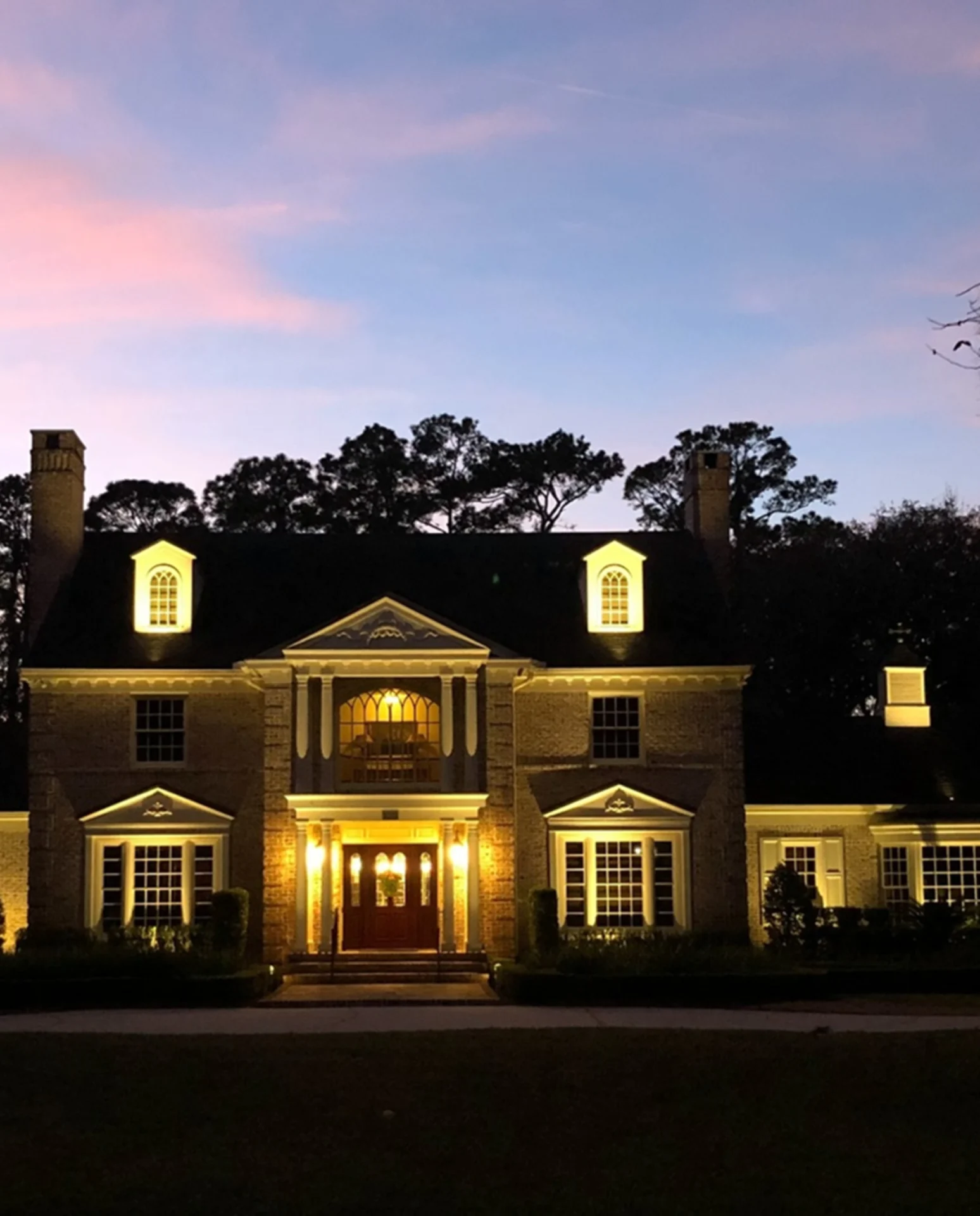 Illuminated house at sunset with trees.